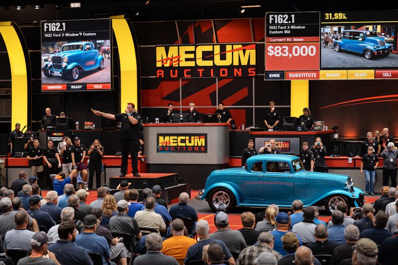 Classic car crossing the block at a Mecum live auction with bidders and auctioneer in action.