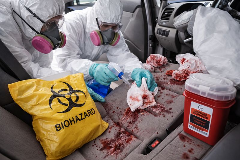Professional biohazard cleaning team wearing protective gear sanitizing a car interior contaminated with biological materials.