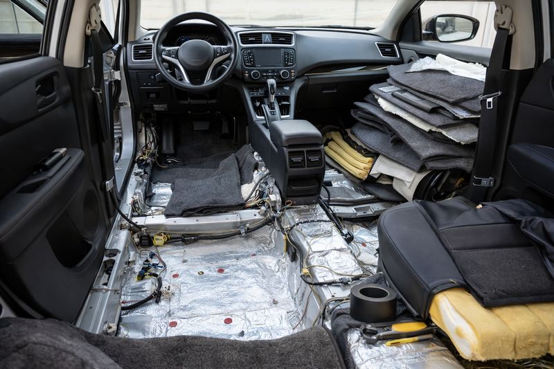 Car interior under restoration after biohazard damage, showing removed seats, carpet, and replacement parts.